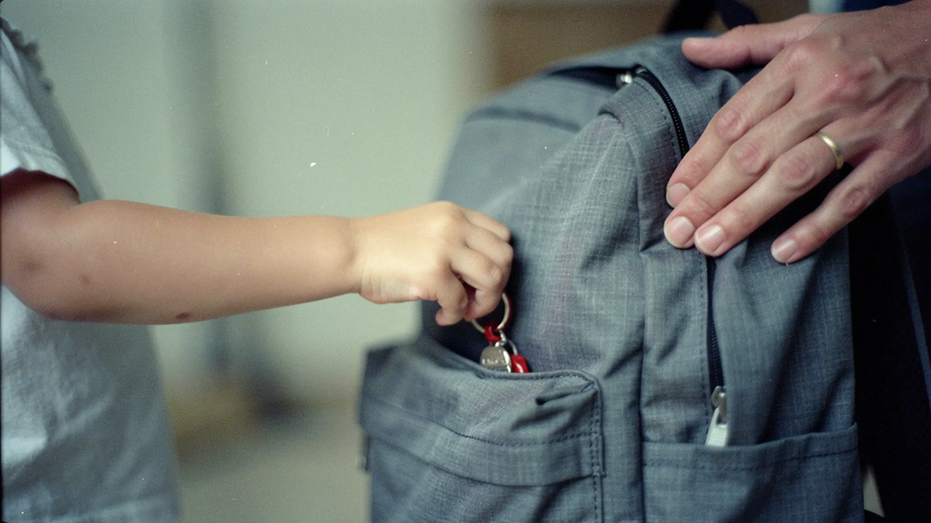 Gros plan sur la main d'un enfant glissant un petit objet réconfortant dans la poche avant de son cartable, la veille de la rentrée