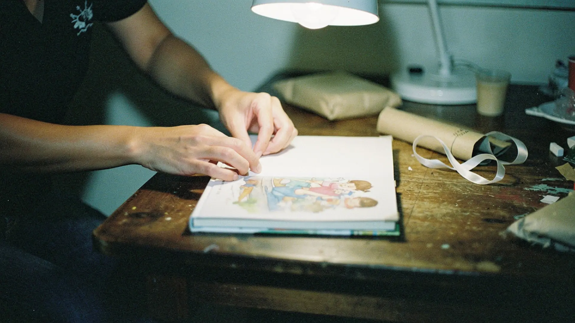 Parent emballant un livre illustré pour enfant sur une table en bois, lumière du soir