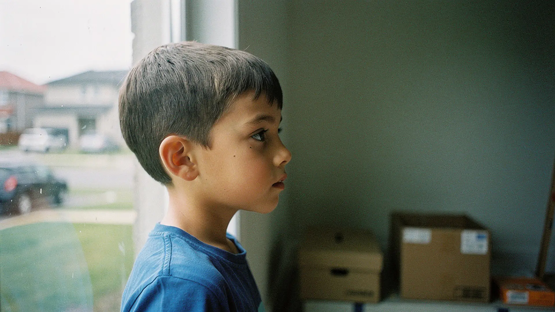 Garçon de 8 ans regardant pensivement par la fenêtre d'une maison inconnue