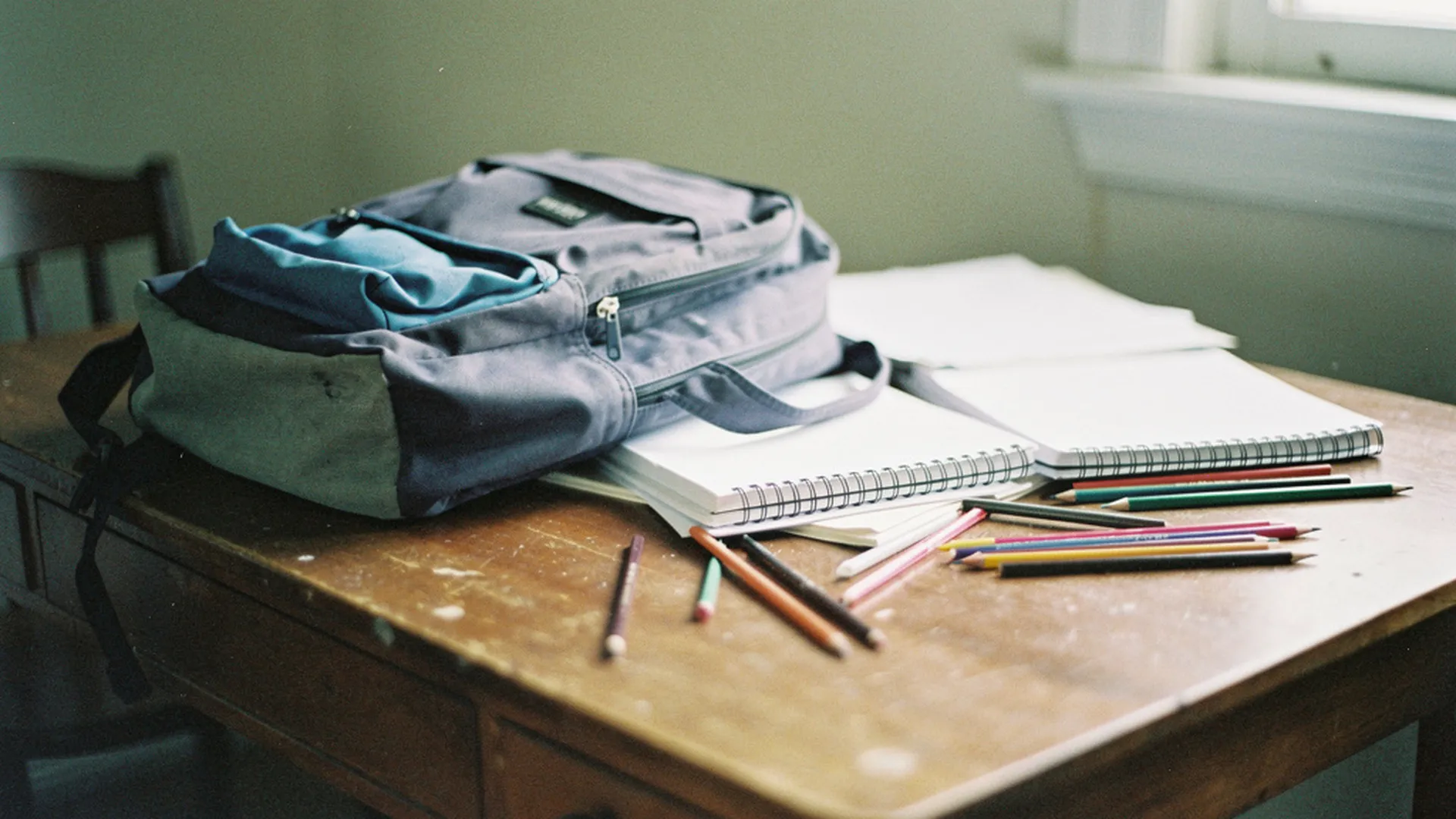 Cartable d'écolier ouvert sur un bureau, cahiers et crayons de couleur éparpillés autour