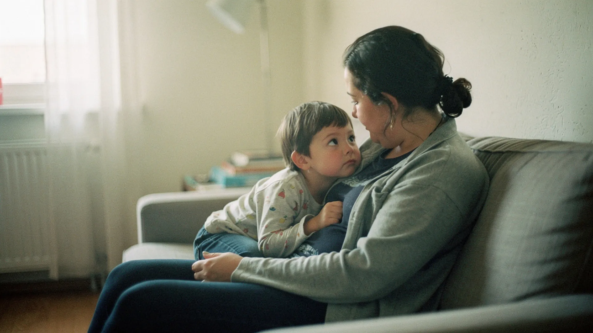 Un parent partage un moment calme en tête-à-tête avec son enfant sur un canapé, à l'écart du reste de la famille