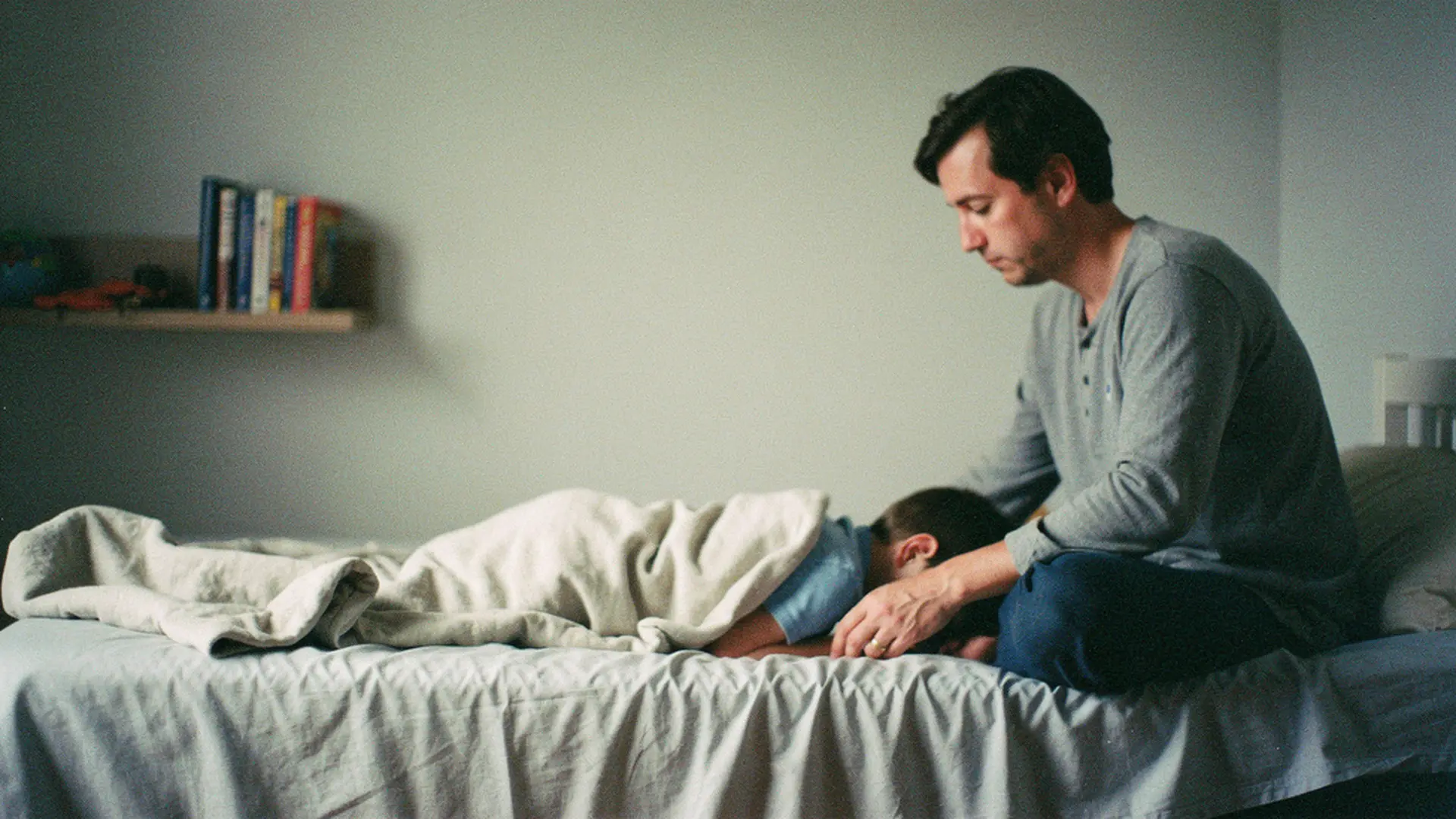 Parent assis au bord du lit d'un enfant qui semble triste, dans une chambre calme le soir