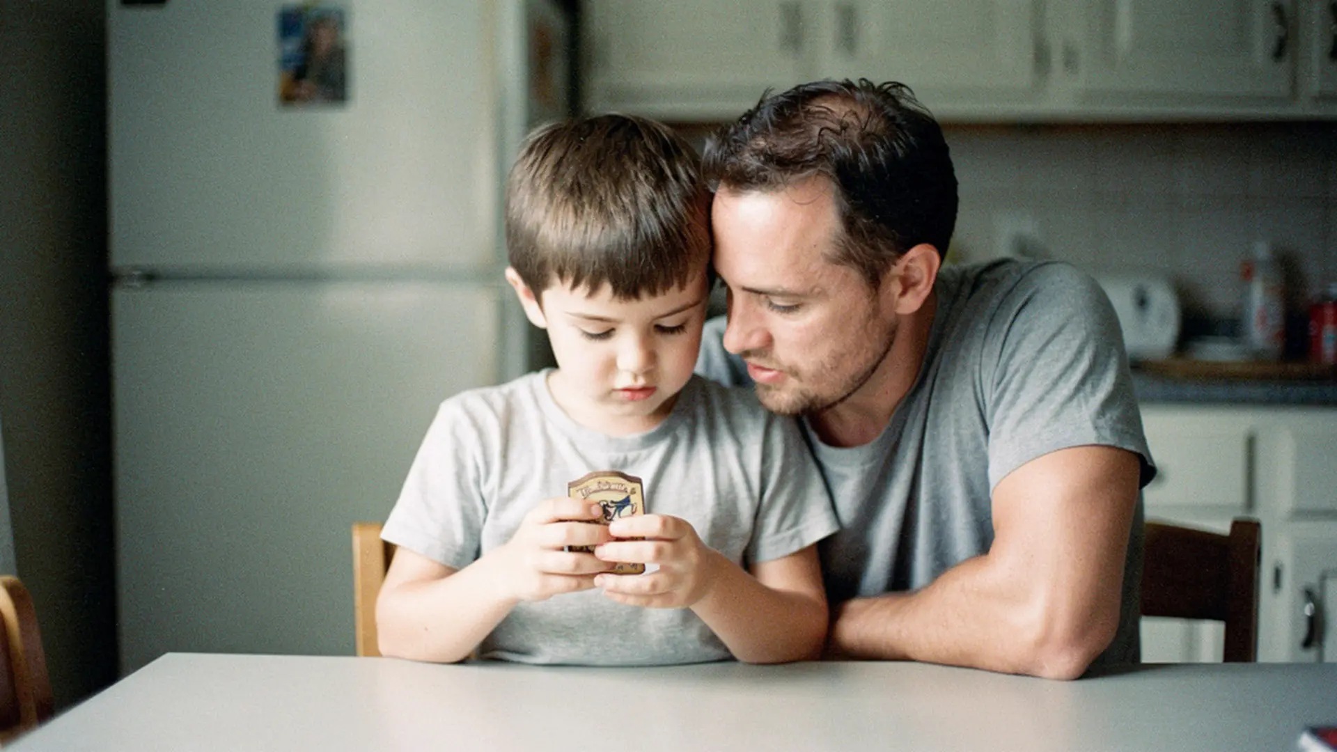 Un père et son fils de 8 ans assis à une table, regardant ensemble un petit objet personnalisé