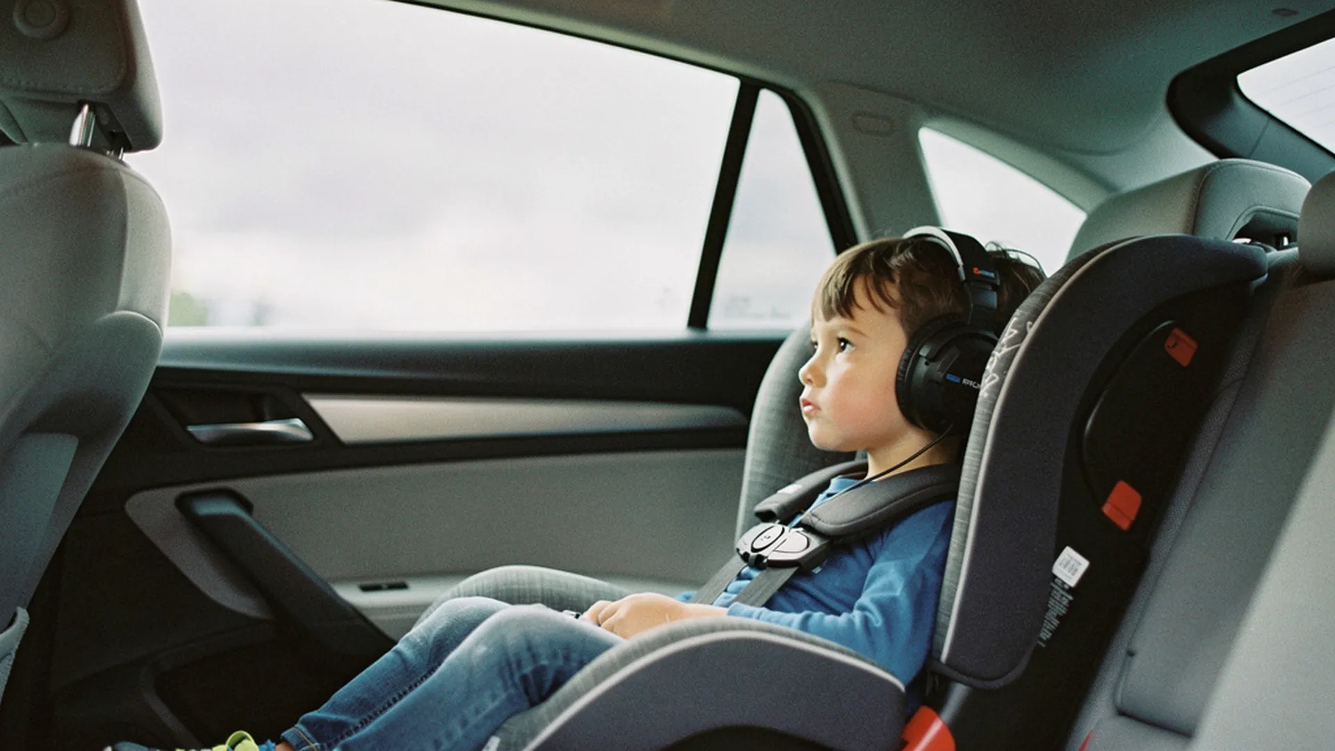 Enfant de 5 ans écoutant une histoire audio dans un siège auto, casque sur les oreilles