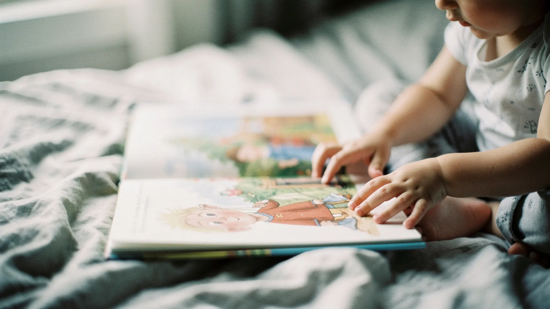 Gros plan sur les mains d'un enfant tournant la page d'un livre illustré posé sur un lit